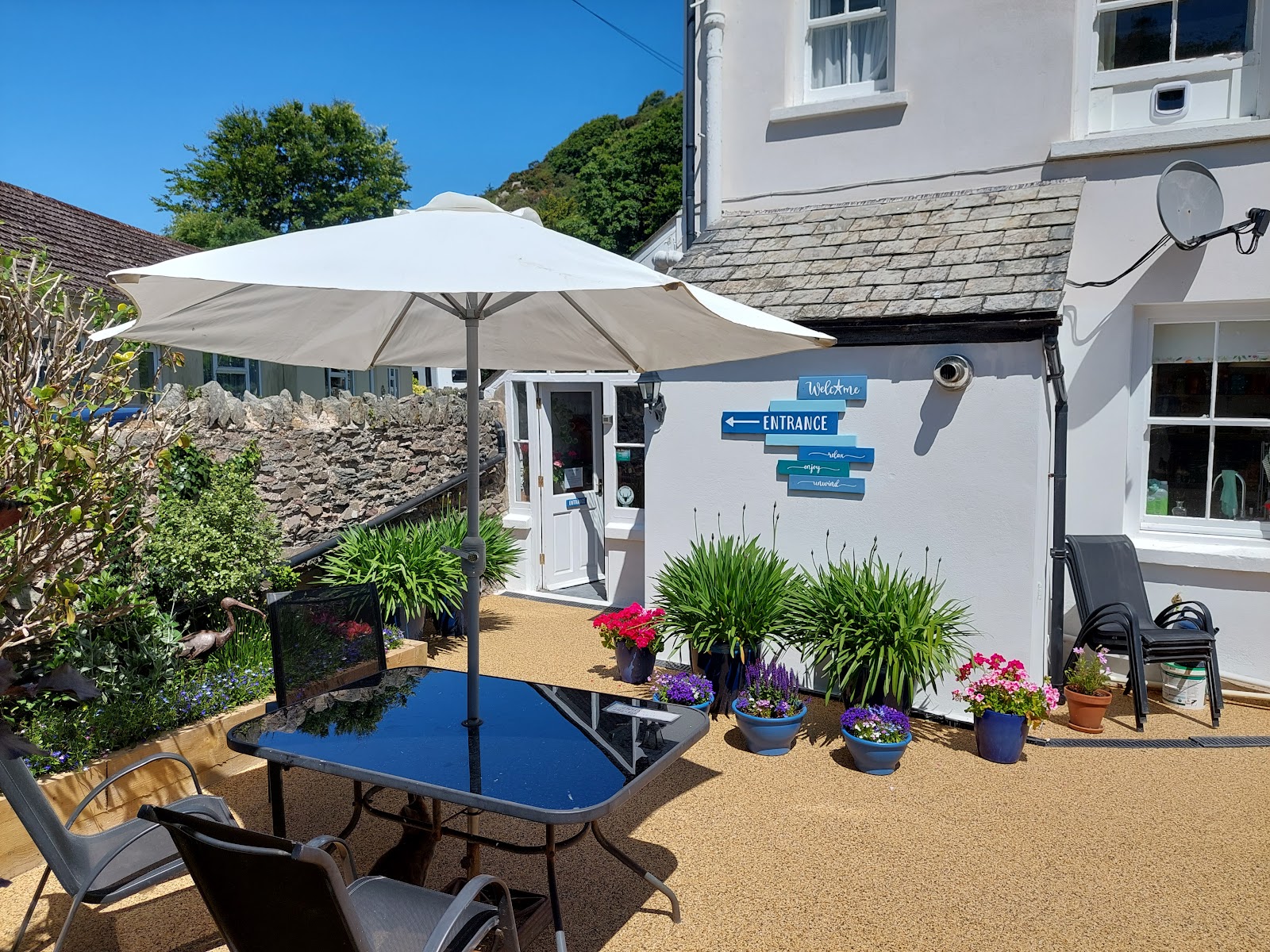 The Denes terrace with its large white parasol, table, chairs and flower planters
